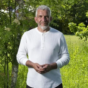 John Millar wearing white top standing in a field with grass and trees