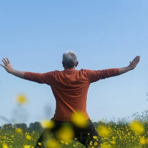 John Millar practising Qi Gong in a field with flowers and blue sky