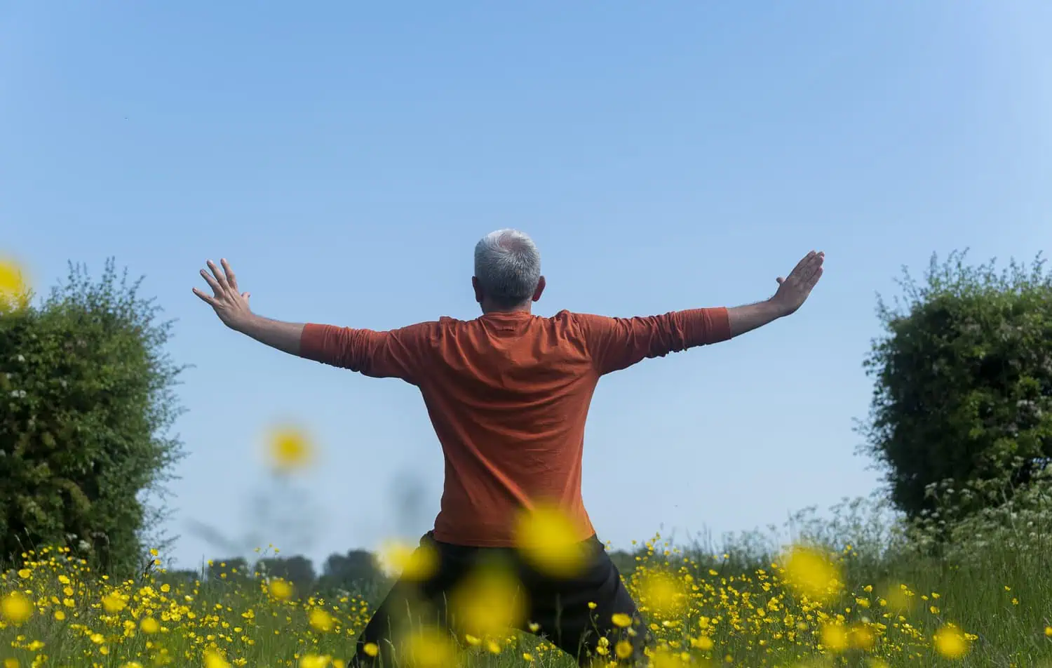 John Millar practising Qi Gong in a field with flowers and blue sky